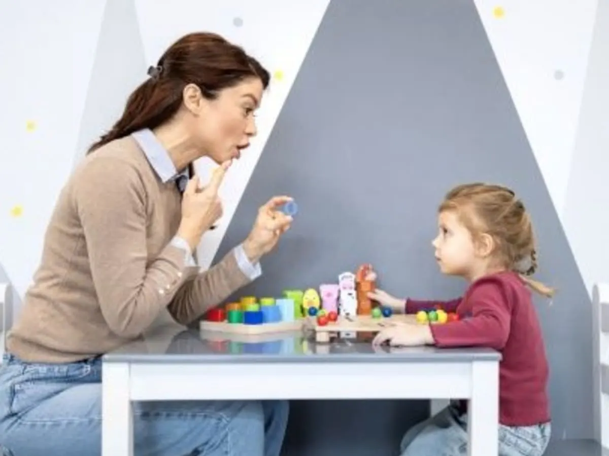 Cette image montre une interaction éducative entre un adulte et un jeune enfant dans un cabinet spécialisé dans l'accompagnement des enfants.