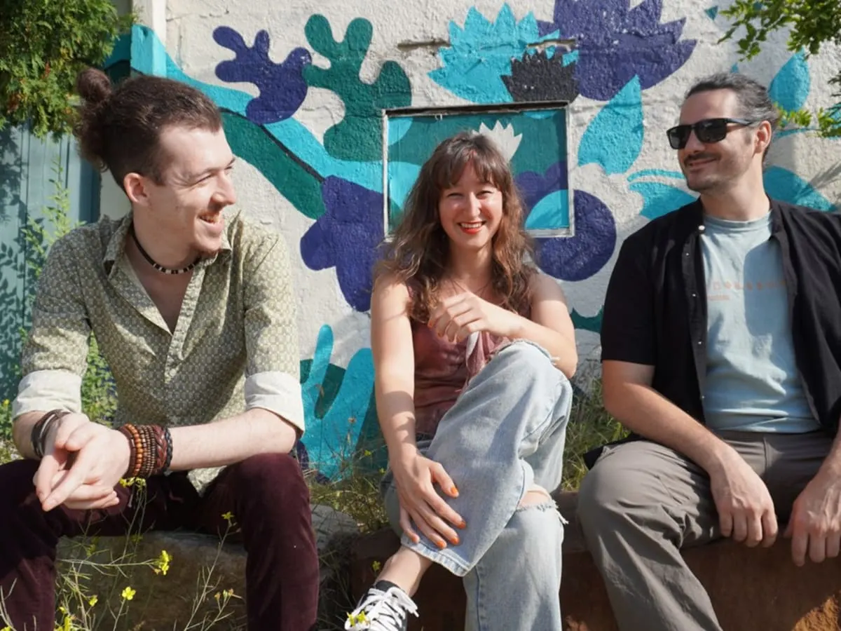 Ariane Racicot et ses 2 musiciens assis devant une murale.