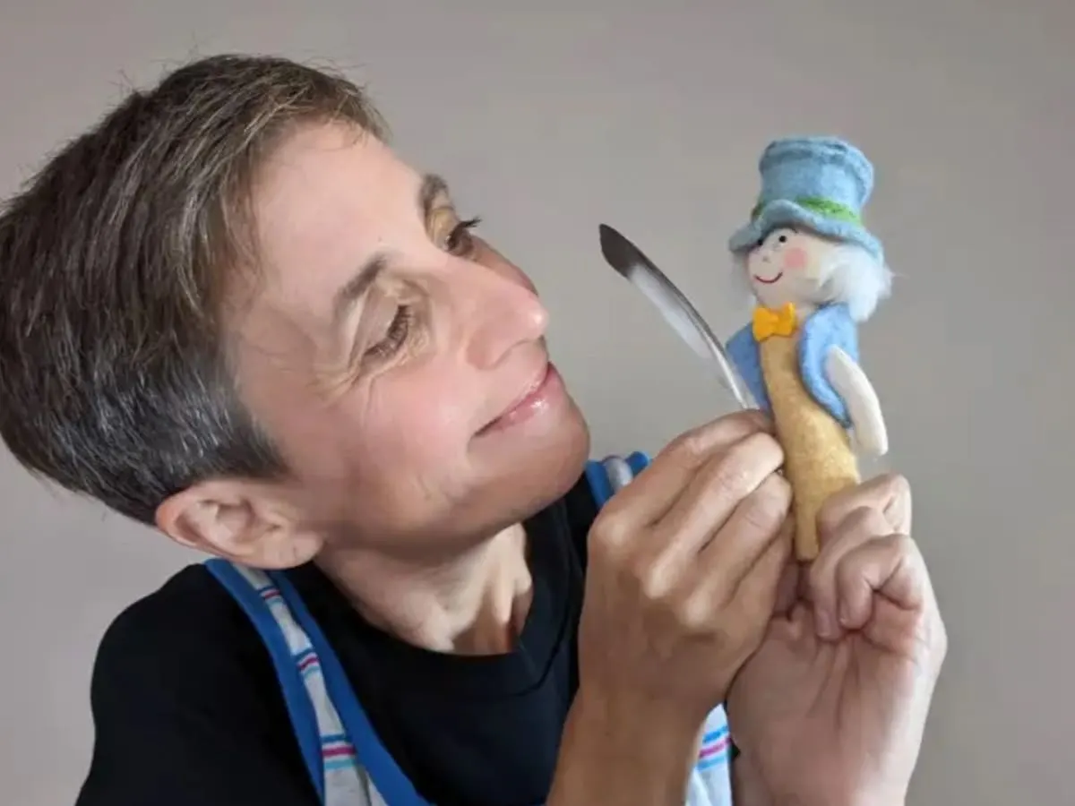 Une femme avec une toute petite marionnette et une plume dans ses mains.