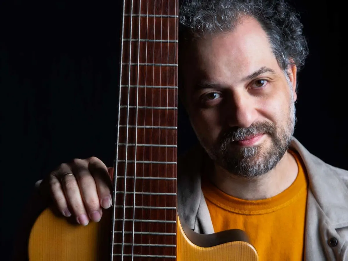 Homme tenant sa guitare près de lui sur fond noir.
