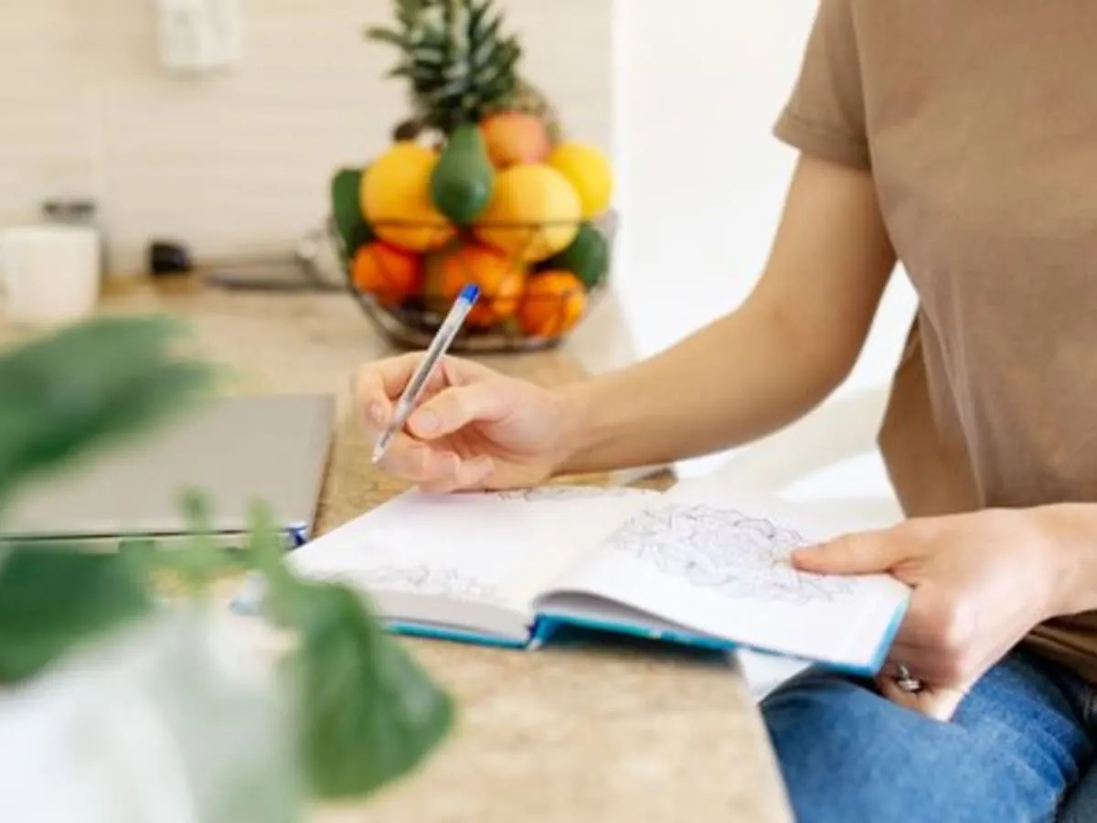 Une personne écrit dans un carnet sur le comptroi d'une cuisine où se trouve des fruits et légumes.