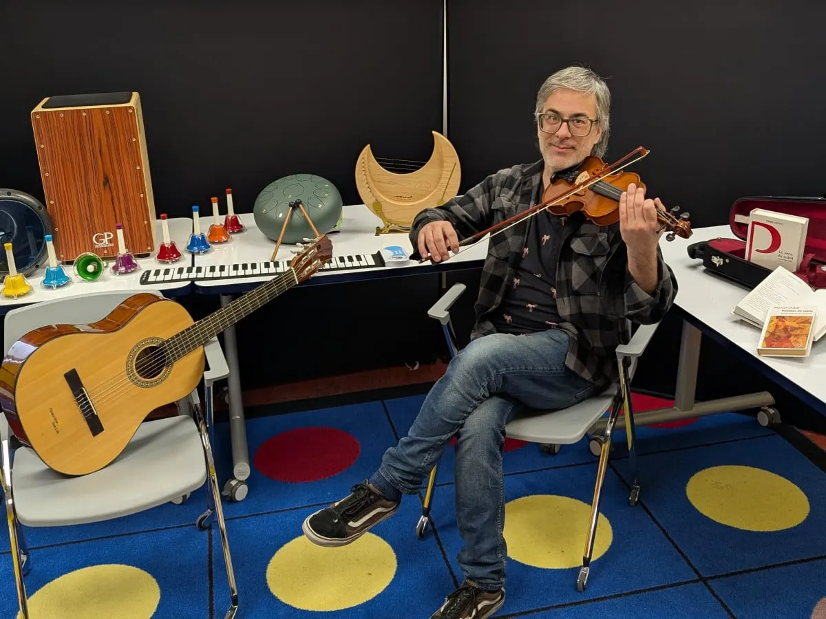 Une personne joue du violon, entourée d'instruments de musique et de livres.
