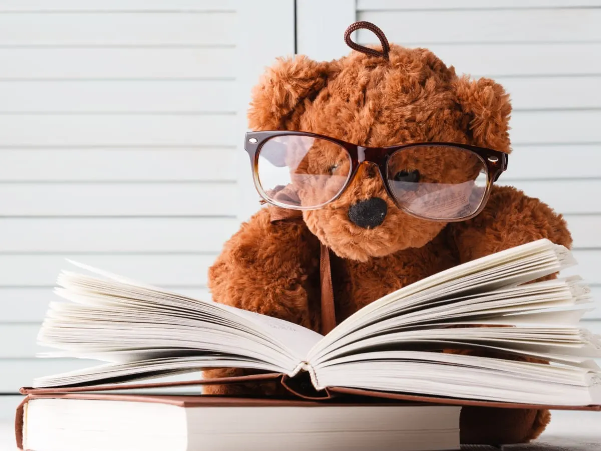 Un ourson avec des lunettes semble lire un livre.