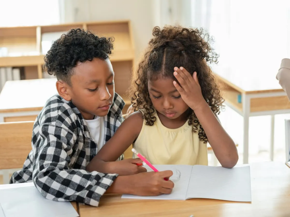 Deux enfants côte à côte regardent un cahier de devoir.