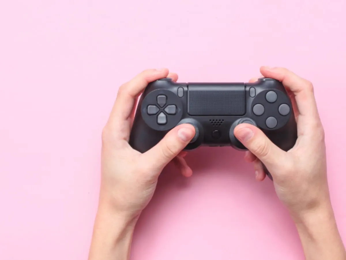 Des mains qui tiennent une manette de jeu vidéo, sur un fond rose.