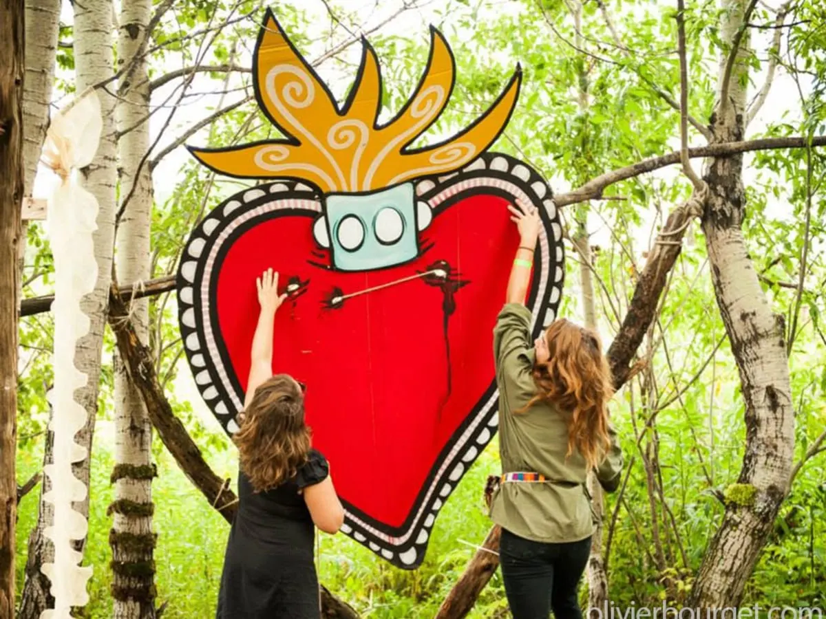 Deux femmes installent un dessin représentant un cœur rouge en forêt.