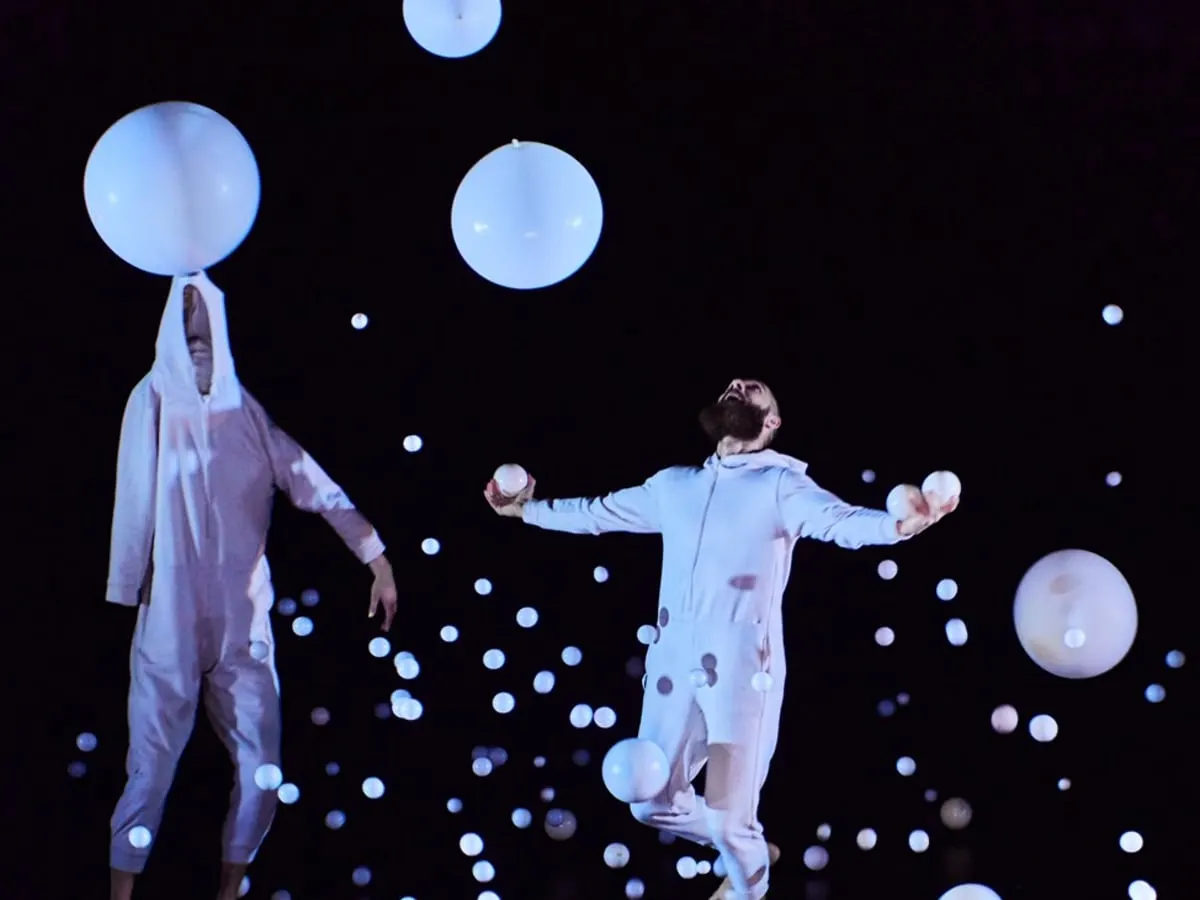 Photo de deux artistes sur scène avec des ballons blancs