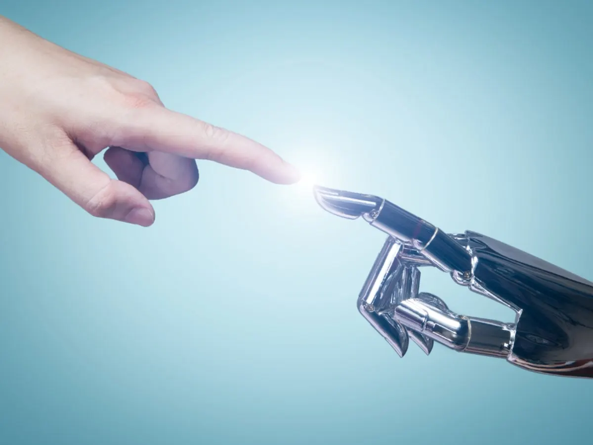 Image de deux mains qui pointent l'une vers l'autre, avec une espèce d'aura lumineuse entre les deux. La main de gauche est la main d'un humain, alors que la main de droite est celle d'un robot métallique.