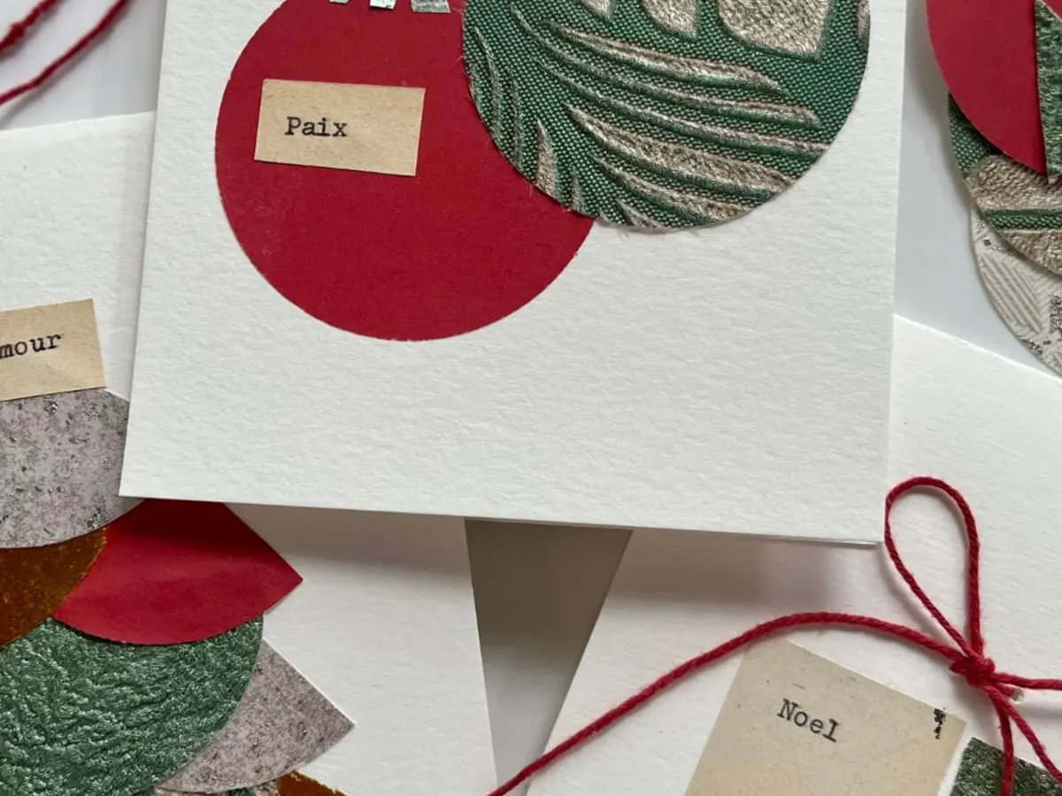 Plusieurs cartes de vœux faites à la main sont décorées de formes colorées en papier et de petits mots comme « Amour », « Paix » et « Noël ». L’image évoque la créativité, le partage et l’esprit des fêtes à travers la confection de cartes personnalisées.