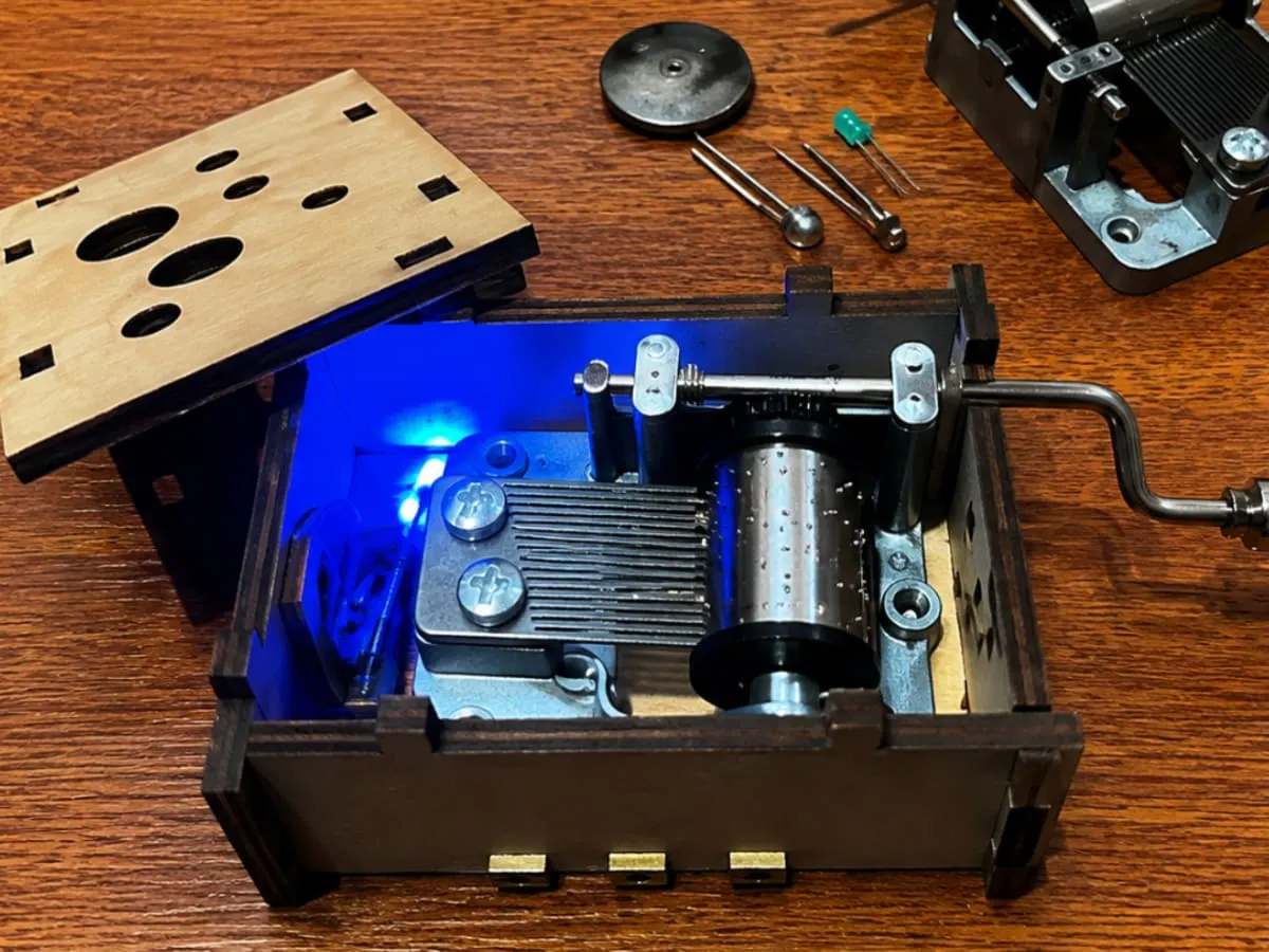 Illustration d’une boîte à musique mécanique ouverte révélant son mécanisme intérieur, avec un cylindre à picots et une manivelle. L’image évoque une activité de découverte où se rencontrent musique, ingénierie et curiosité scientifique.