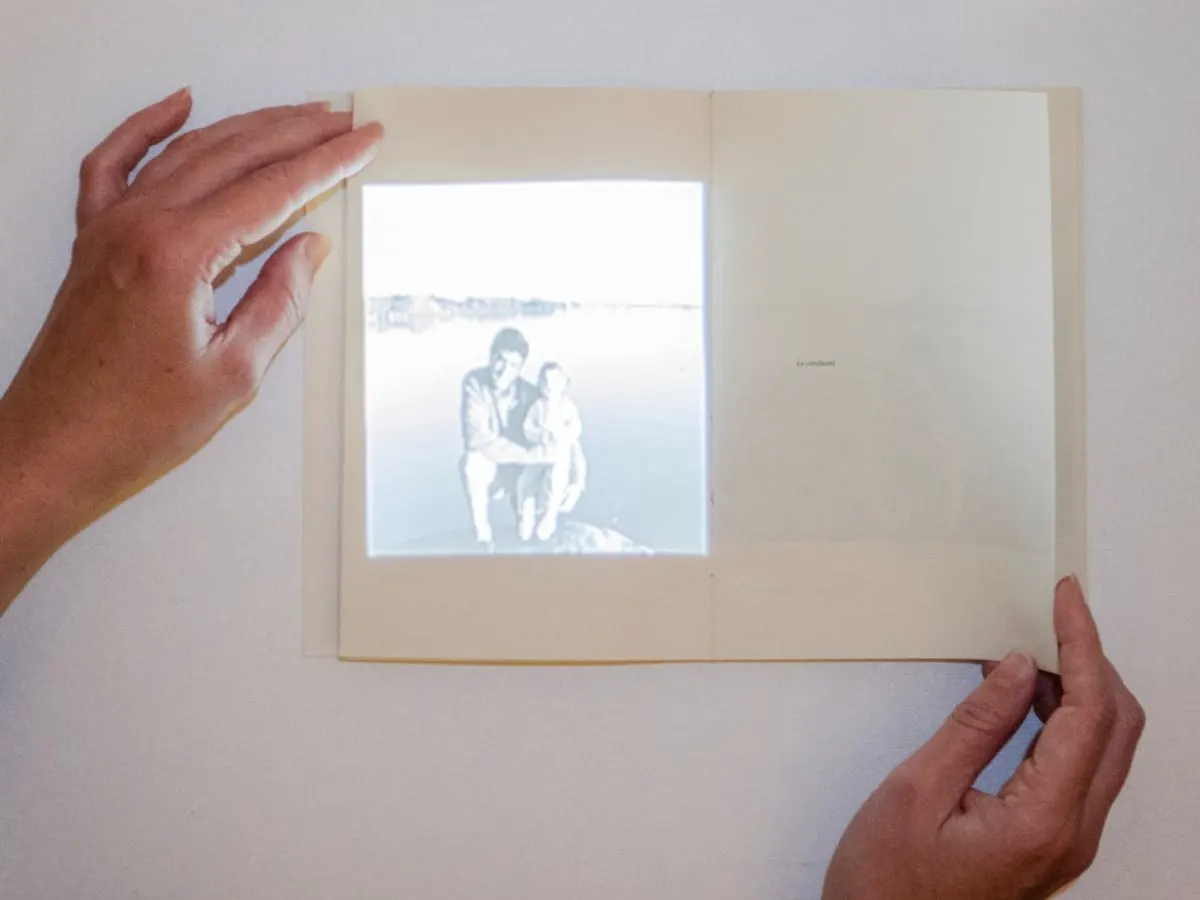 Des mains tiennent un cahier blanc sur lequel la projection d'une photo est faite.
